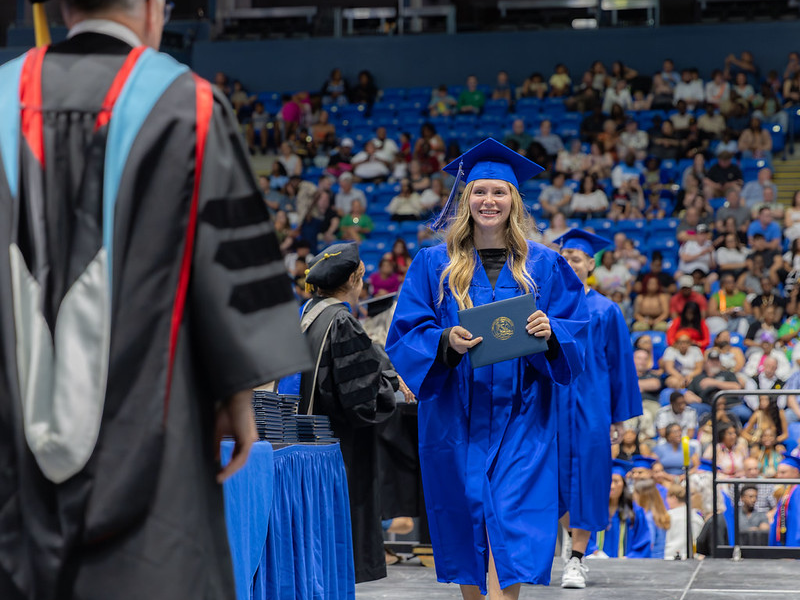 A student in regalia walking with her diploma during commencement