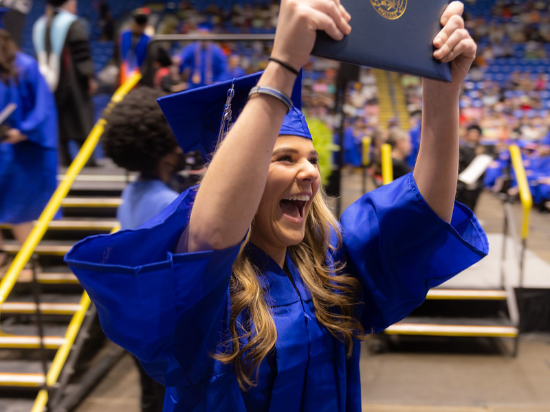 A photo of a graduate smiling and holding her diploma high above her head
