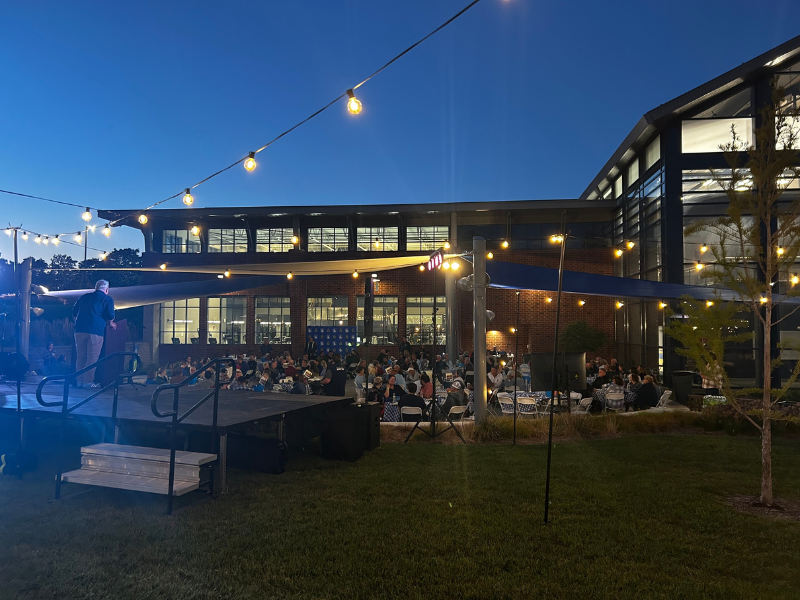A nighttime picture of the Dobski Family Plaza lighted with string lights and filled with people
