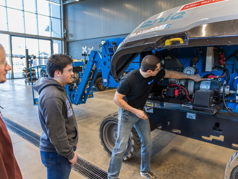A photo of an instructor showing a student something with a diesel engine