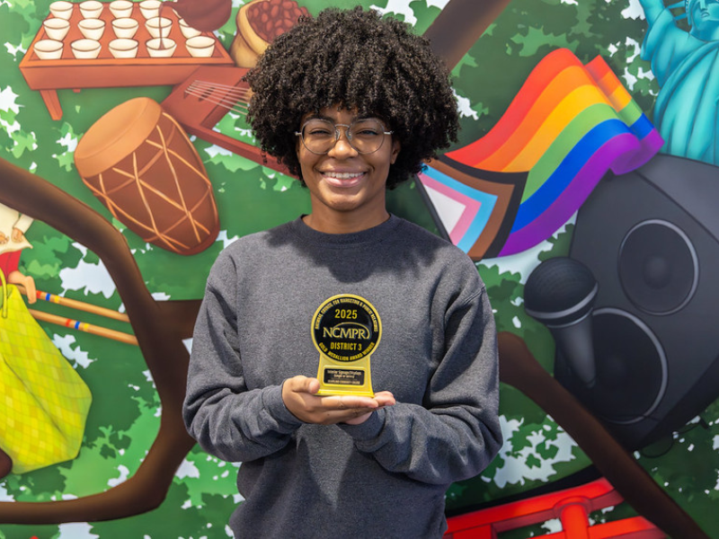A picture of a woman holding an award in front of a colorful mural