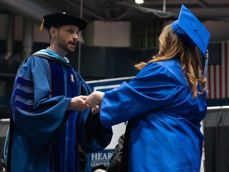 Photo of faculty member presenting diploma cover to a graduate on stage